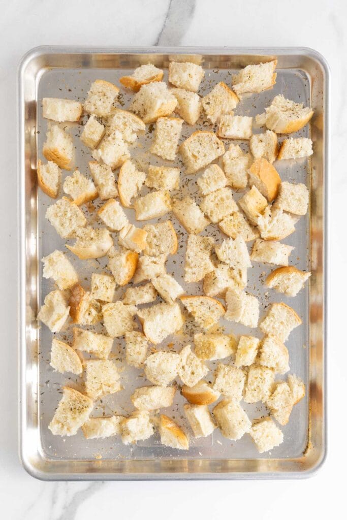 Baking sheet with cubed bread seasoned with herbs, ready to be toasted for croutons