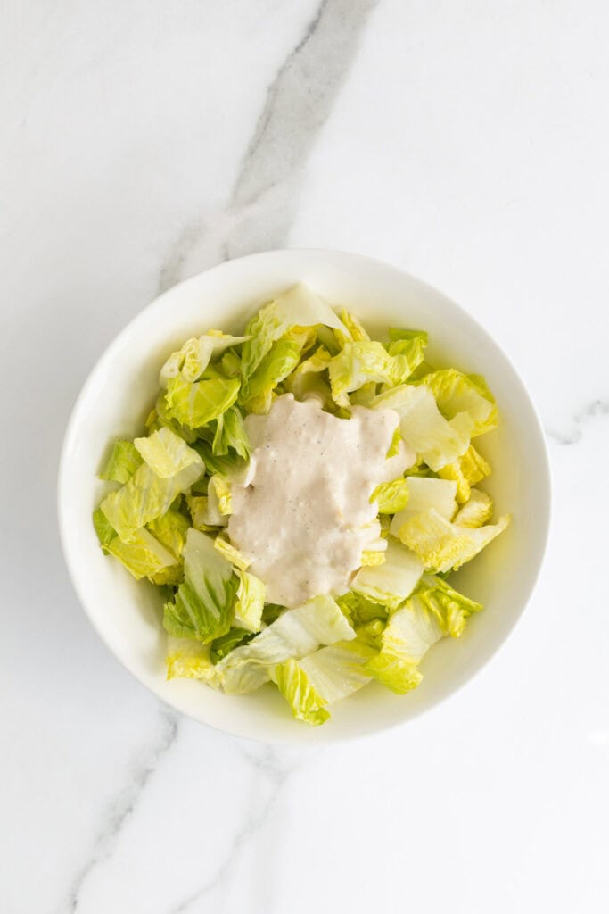 Romaine lettuce in a bowl topped with Caesar dressing before mixing