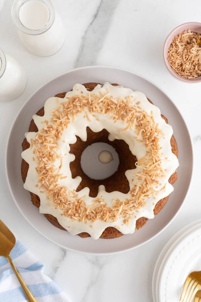 Carrot bundt cake topped with white glaze and sprinkled with toasted coconut, served on a white plate