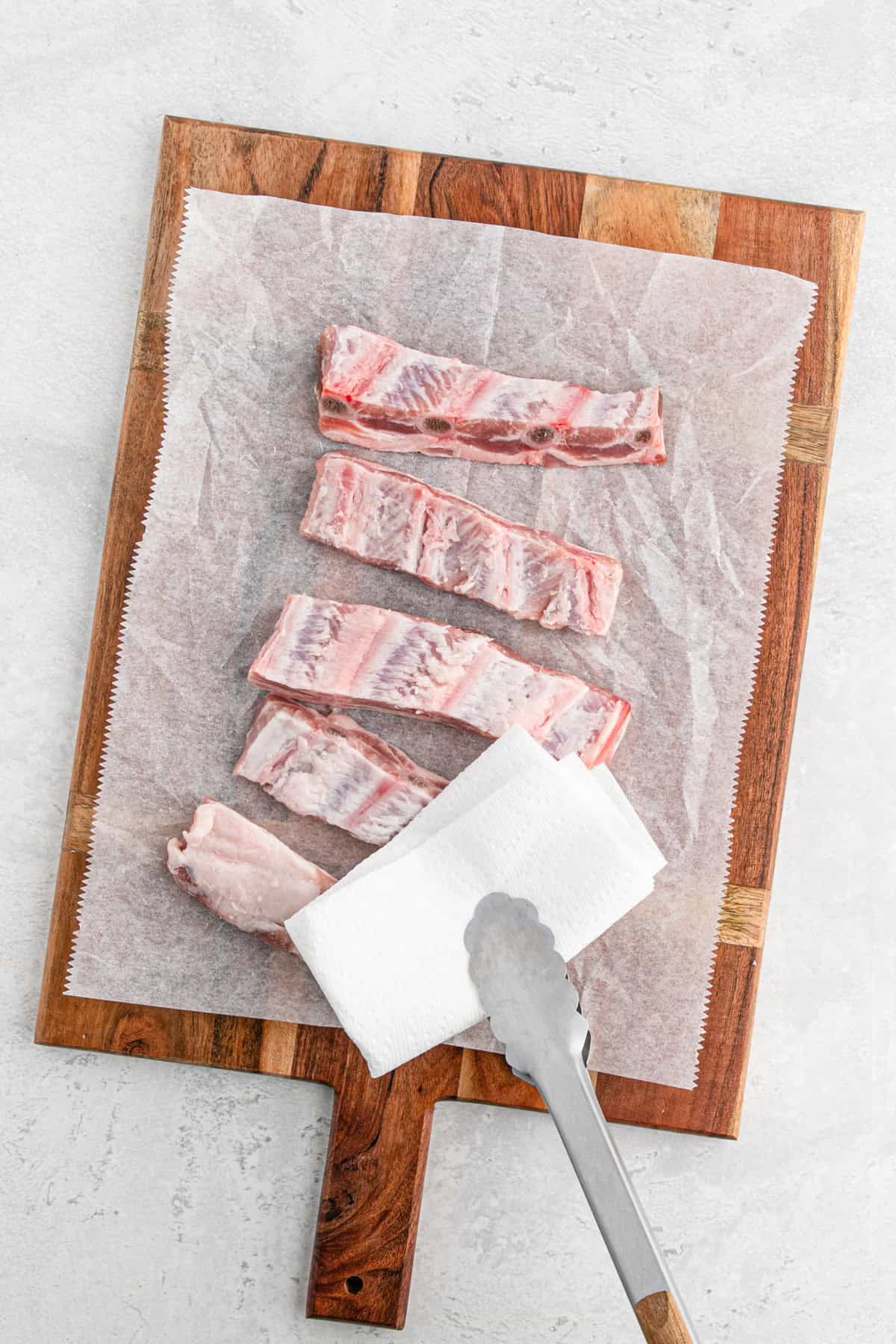 Raw rib tips on parchment-lined butcher paper with paper towels and tongs for drying