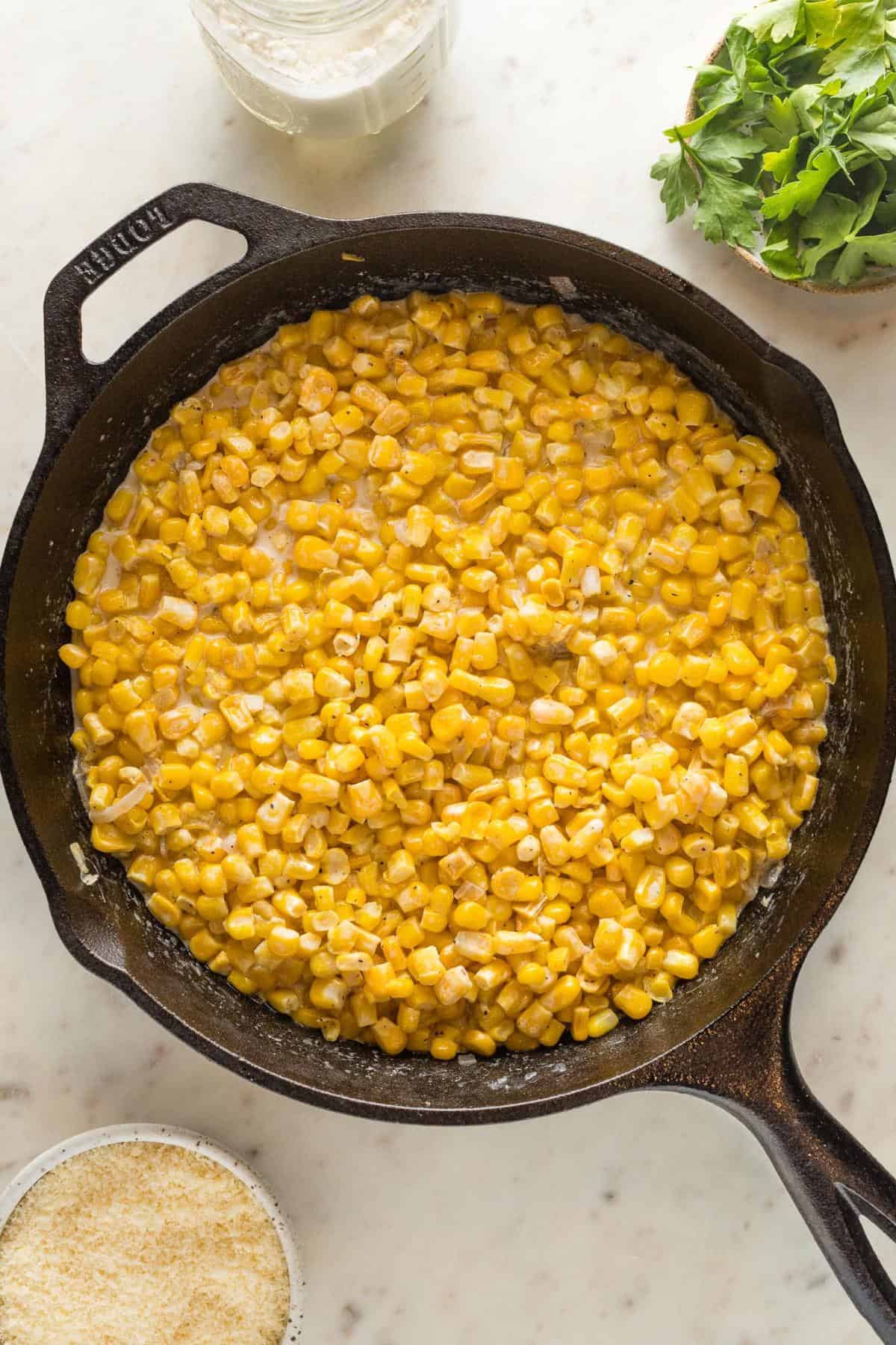 Sweet corn cooking with cream and seasonings in a cast iron skillet before thickening