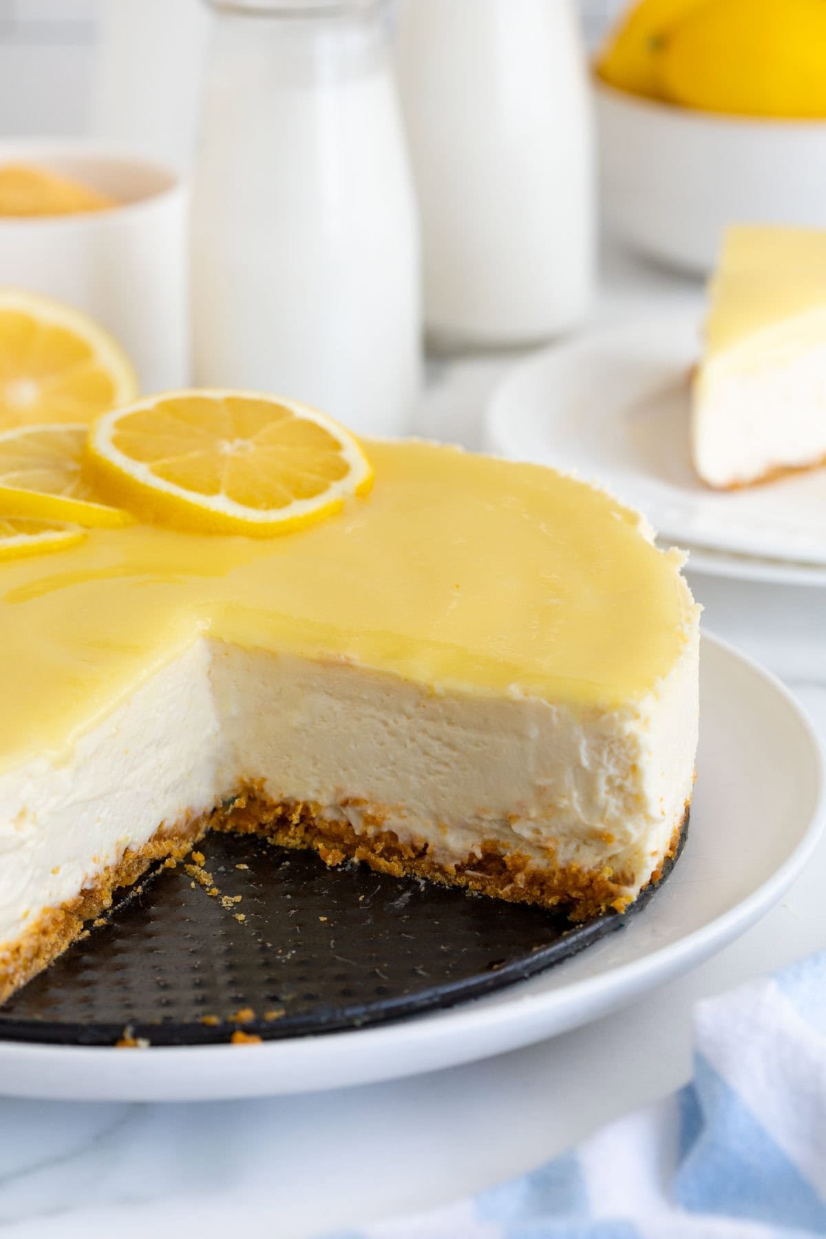 Closeup side view of a lemon cheesecake with a slice removed, showing the creamy texture and graham cracker crust