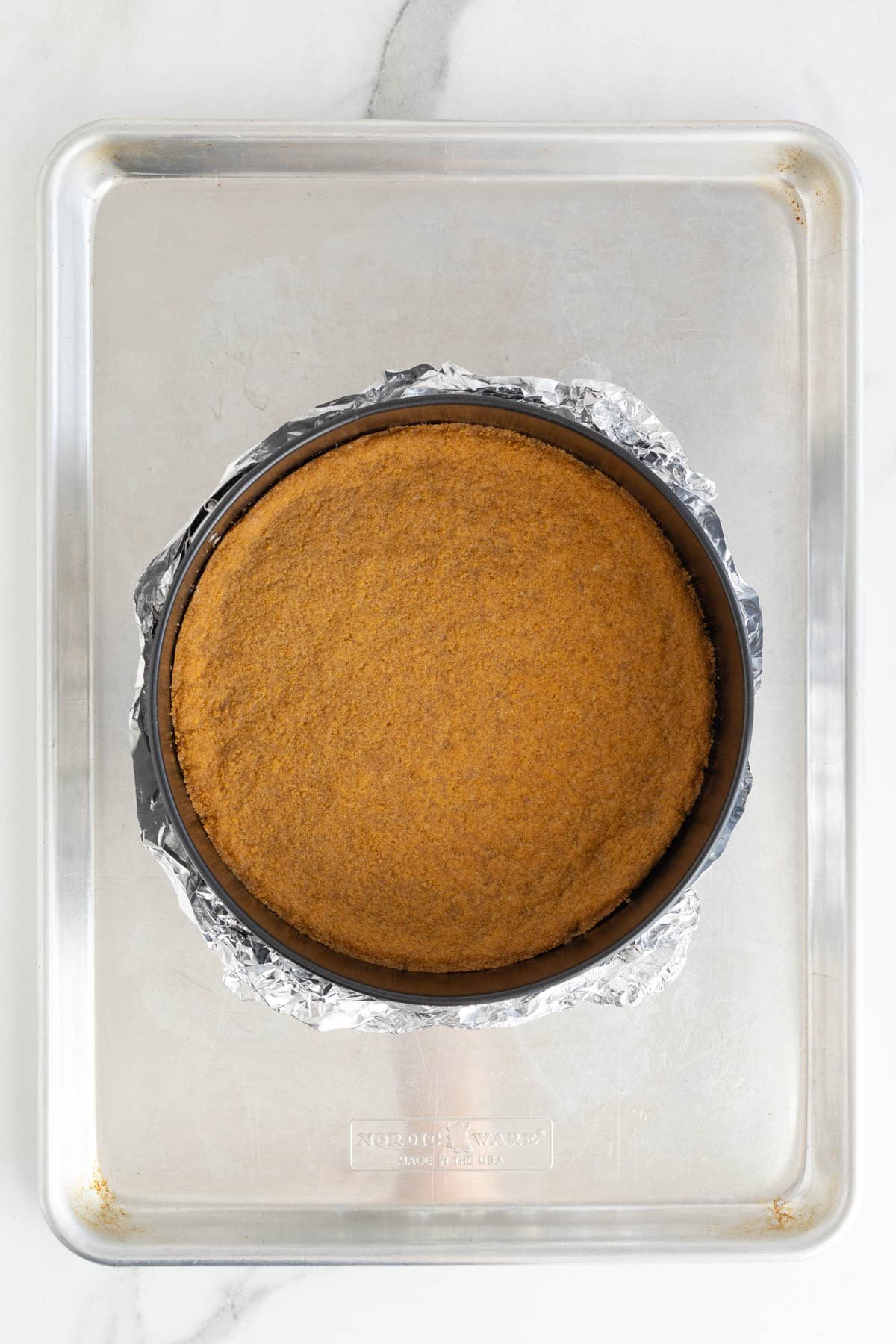 Baked graham cracker crust in a springform pan lined with foil, placed on a baking sheet