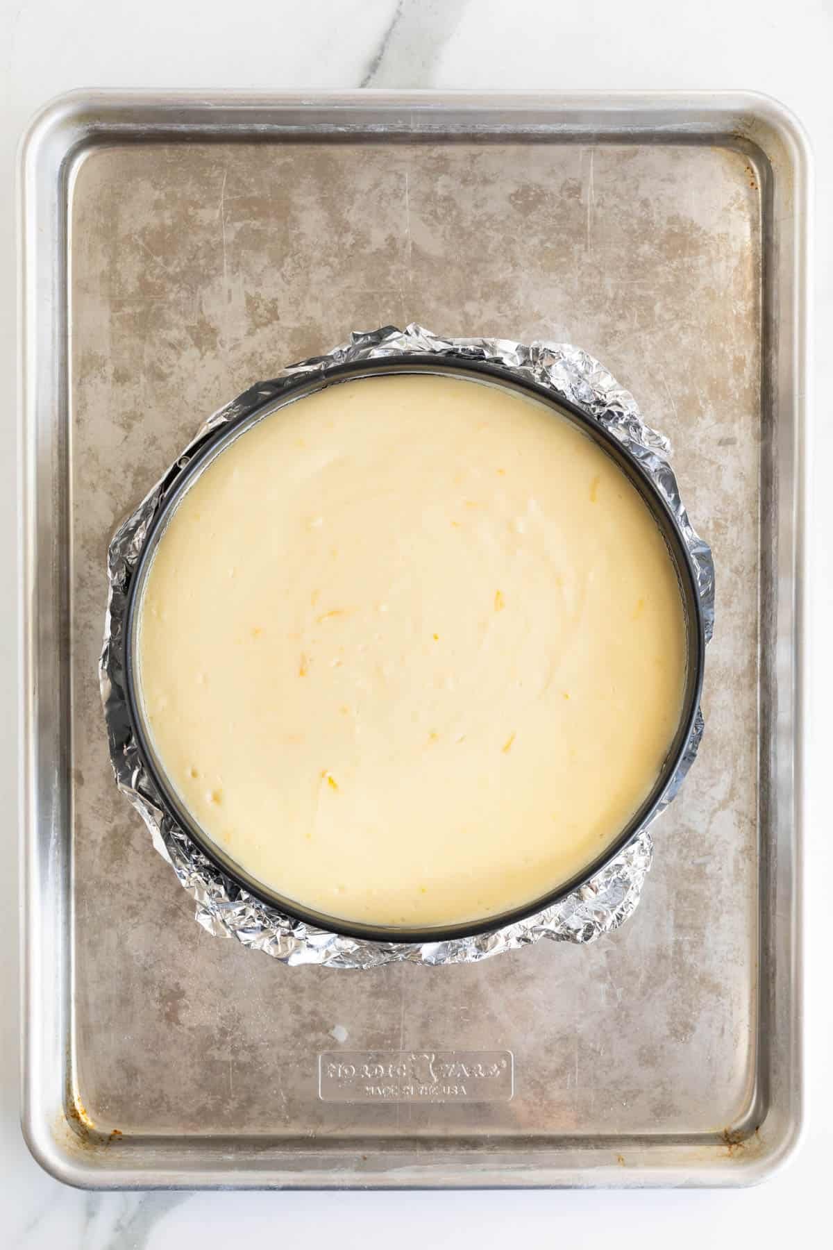 Fully baked lemon cheesecake still in the springform pan, cooling on the baking sheet