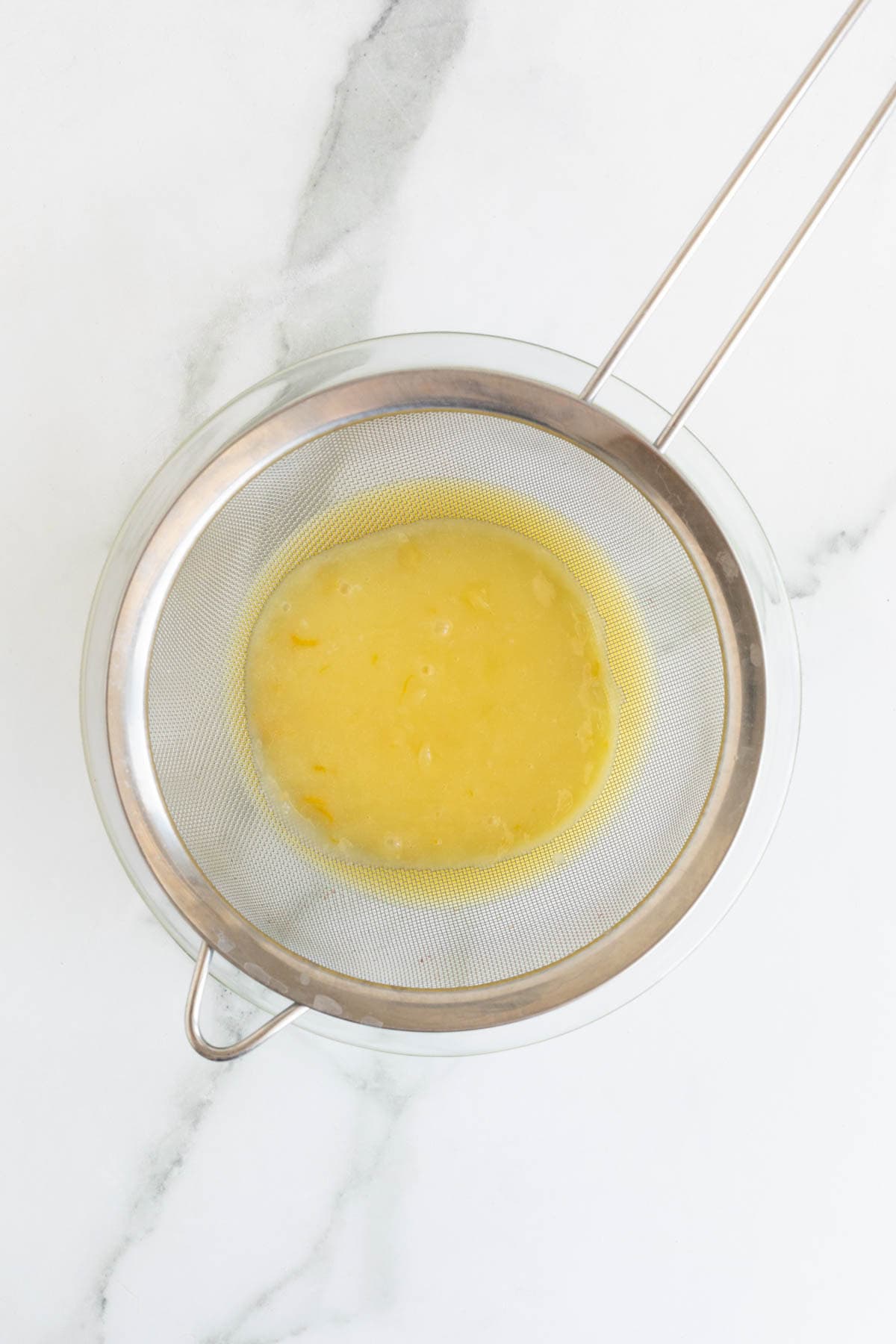 Straining the lemon curd through a fine mesh sieve into a bowl