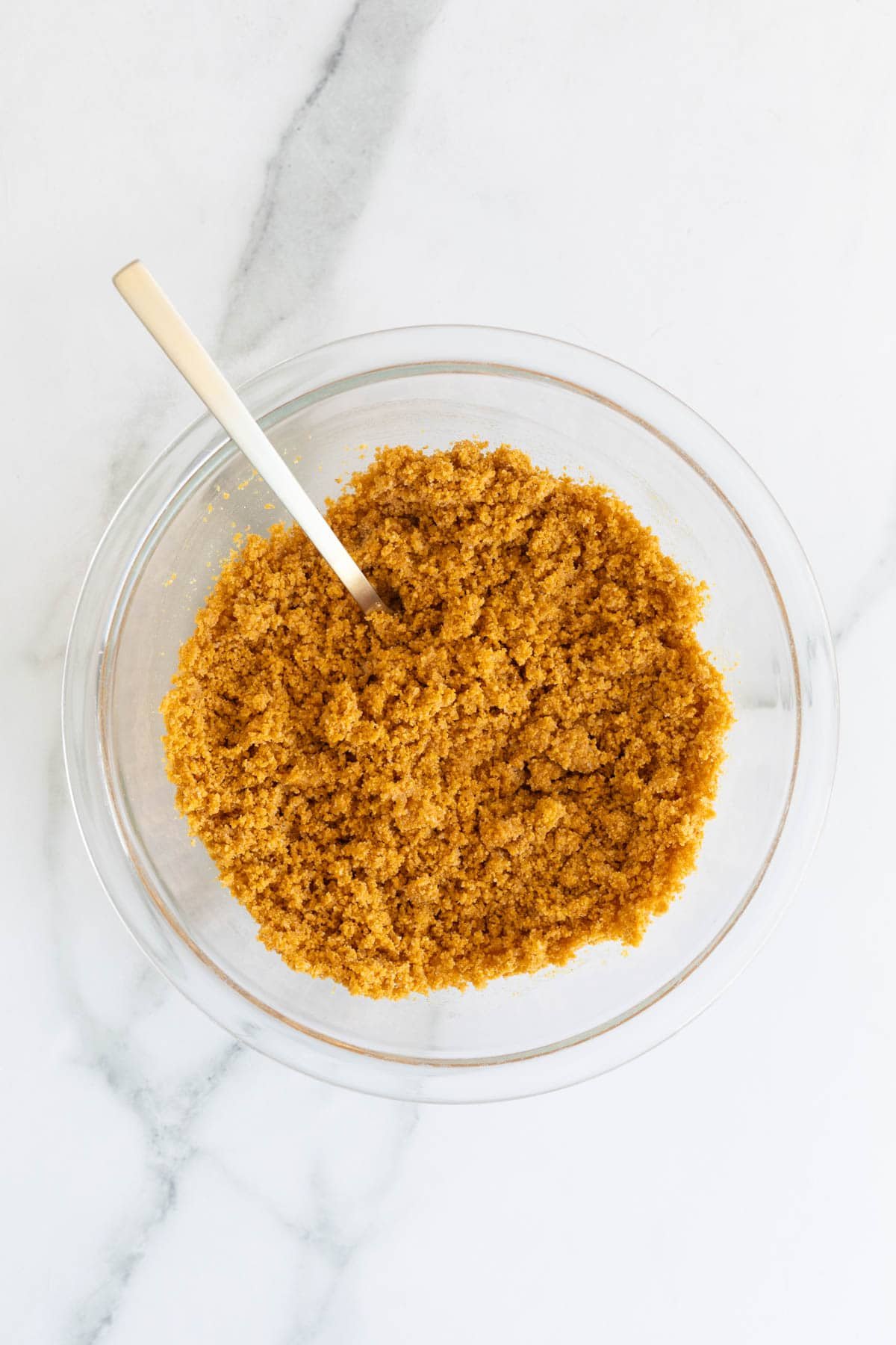 Graham cracker crust mixture fully combined in a glass bowl with a spoon inside