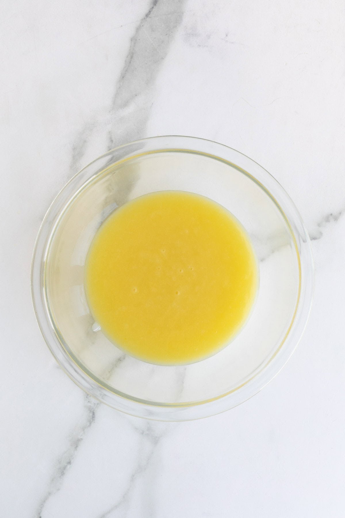 Smooth lemon curd collected in a glass bowl after straining