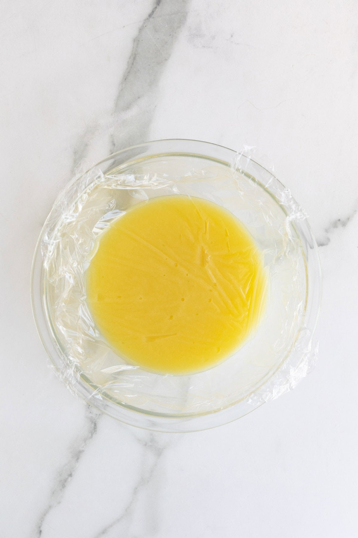 Lemon curd covered with plastic wrap pressed directly on the surface