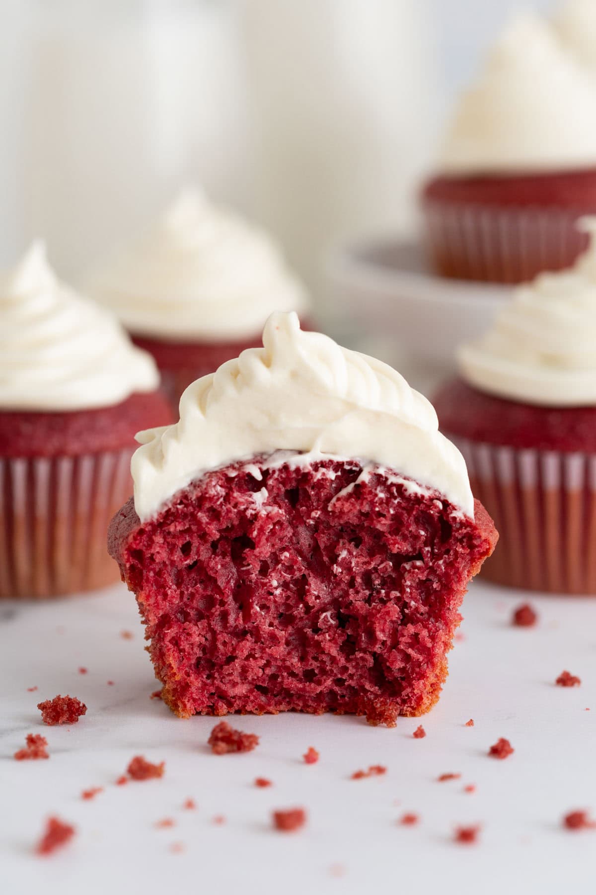 A red velvet cupcake sliced in half to reveal the soft, fluffy interior, with cream cheese frosting on top and crumbs scattered around