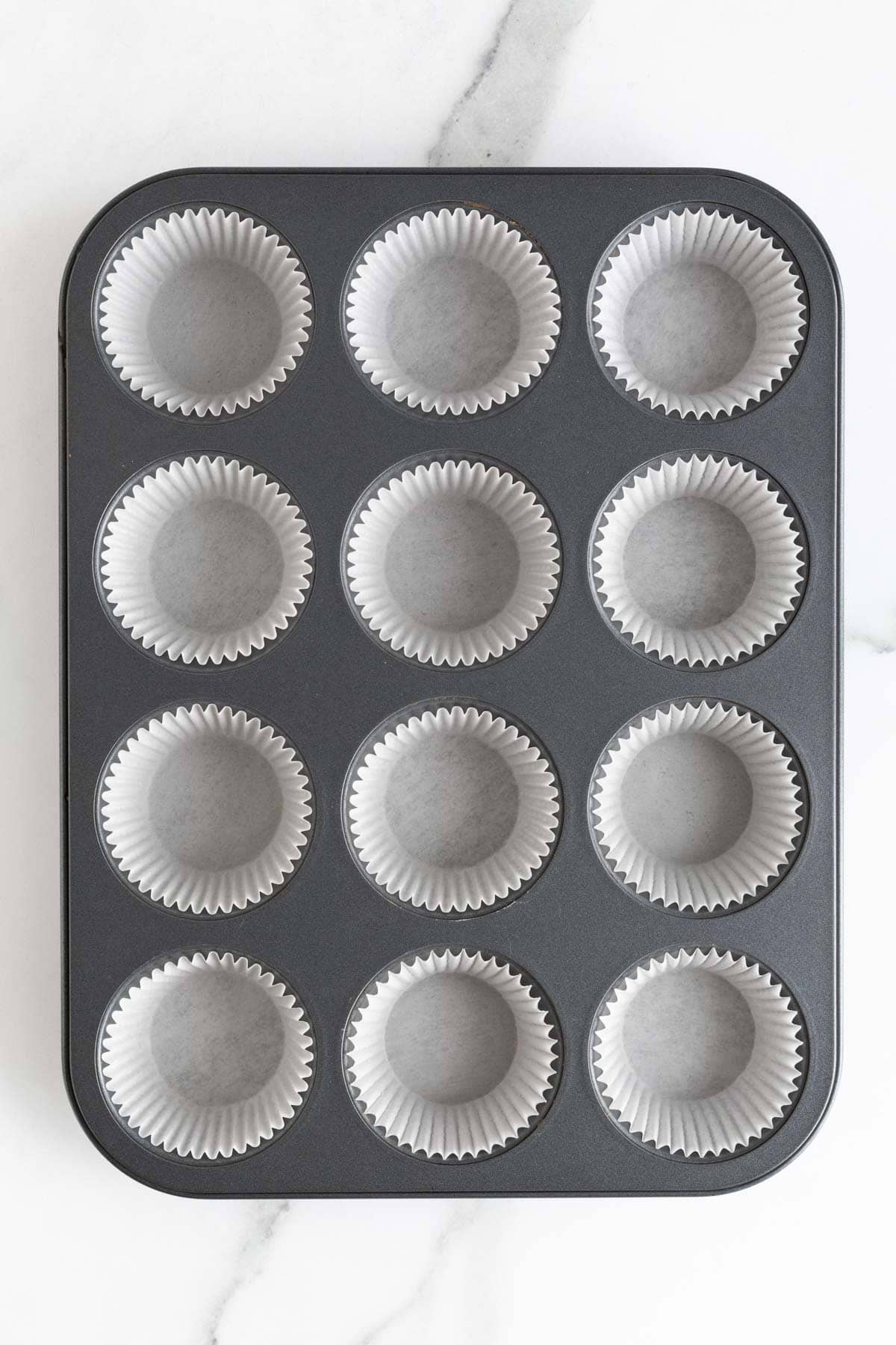 A standard 12-cup muffin pan lined with white cupcake liners, ready for batter