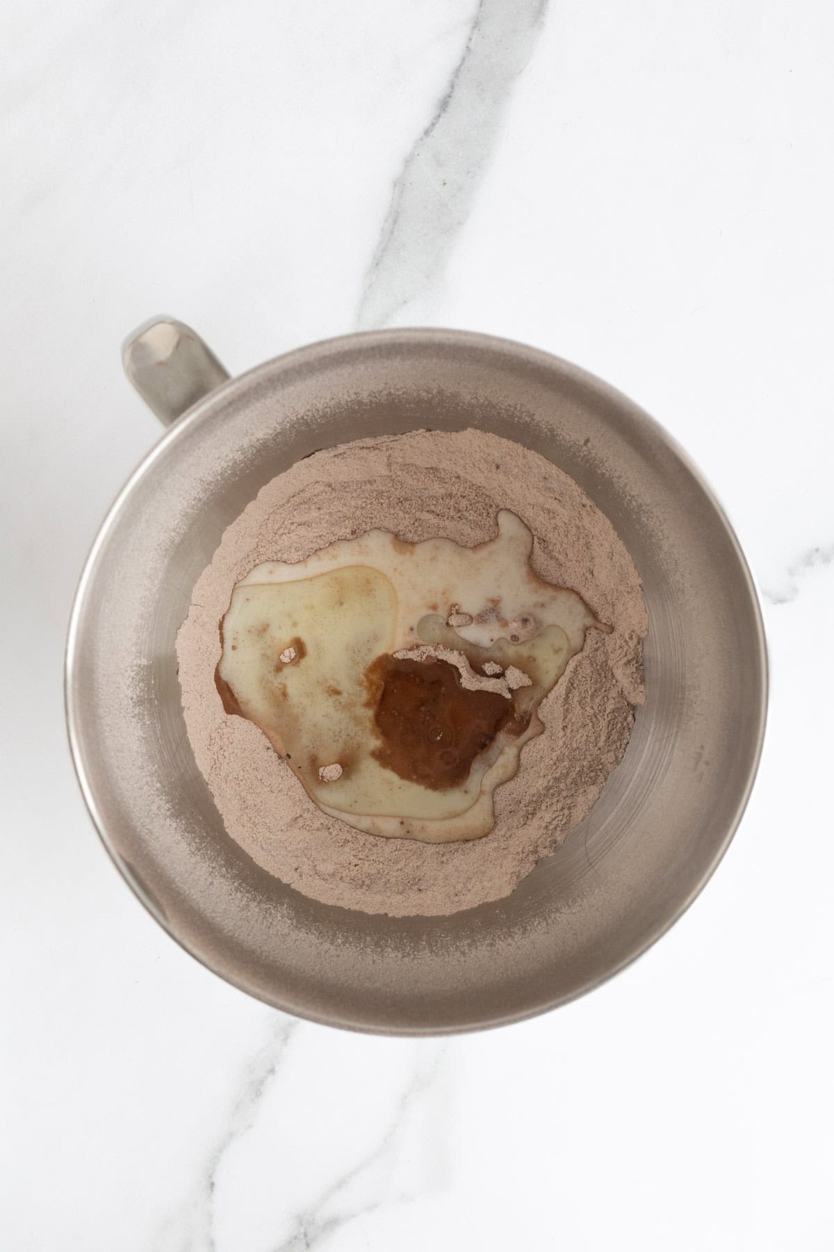 Wet ingredients, including vanilla and buttermilk, poured over the dry mixture in a mixing bowl