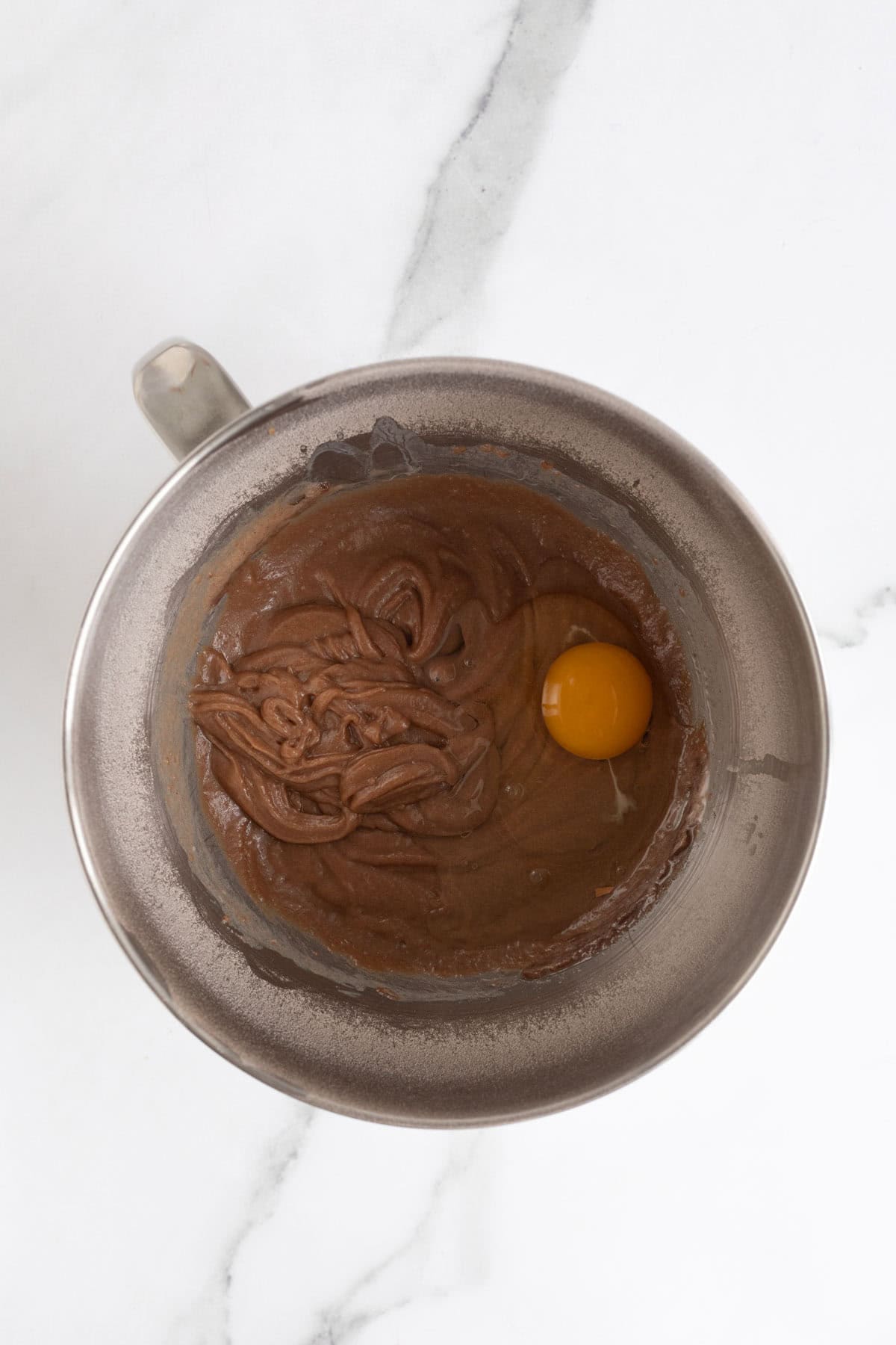 A metal bowl with thick chocolate batter and an egg added in, ready to be mixed