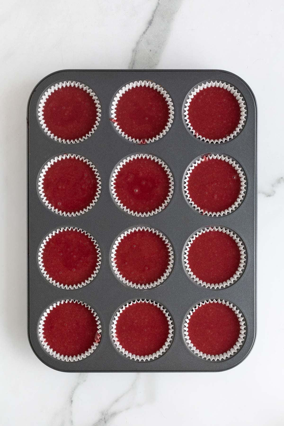 Muffin pan filled with red velvet cupcake batter in liners, ready for the oven