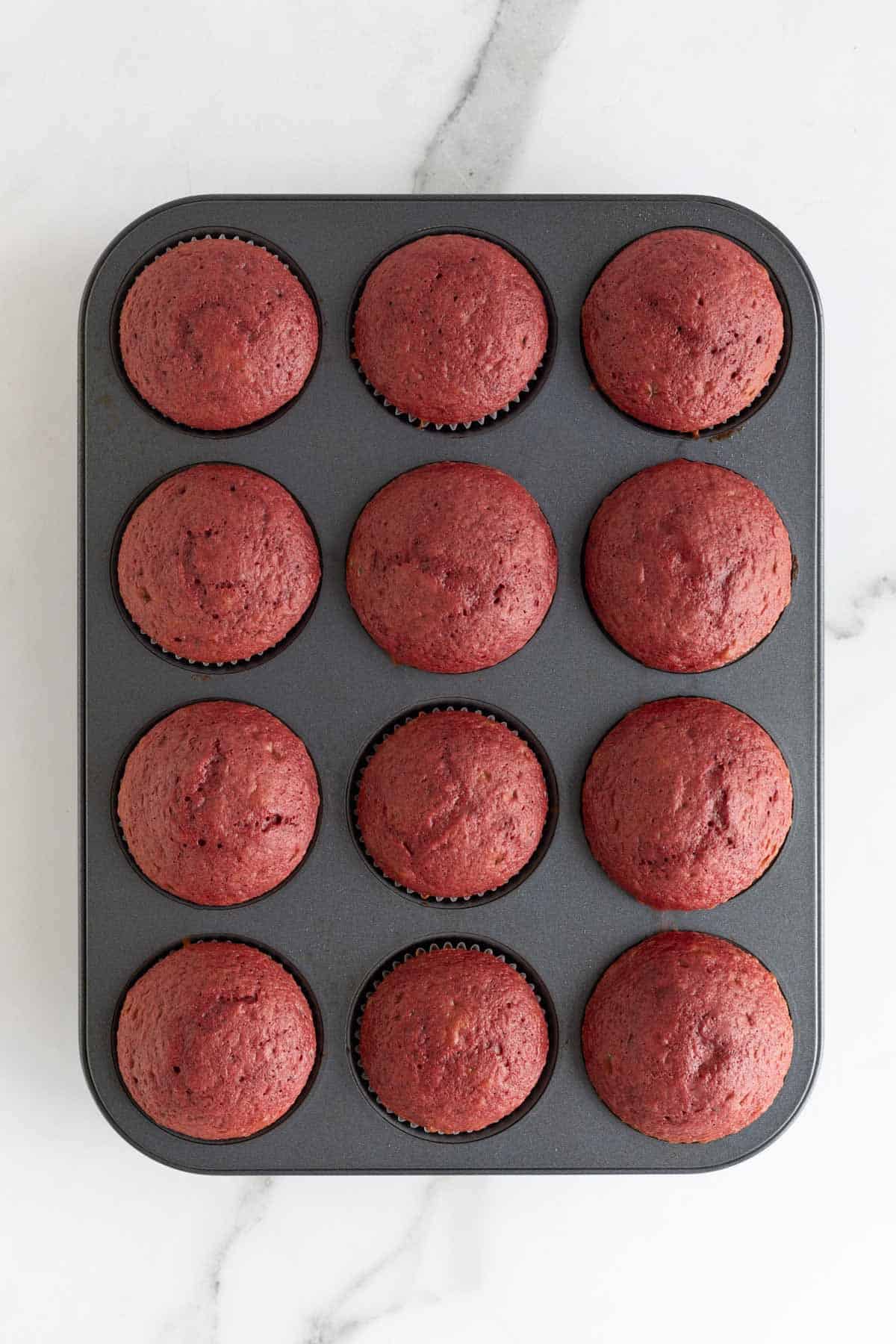 Freshly baked red velvet cupcakes in a muffin tin, domed and set, just out of the oven