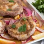 Closeup of sheet pan pork chops with red onions and apples on a sheet pan, topped with parsley leaves