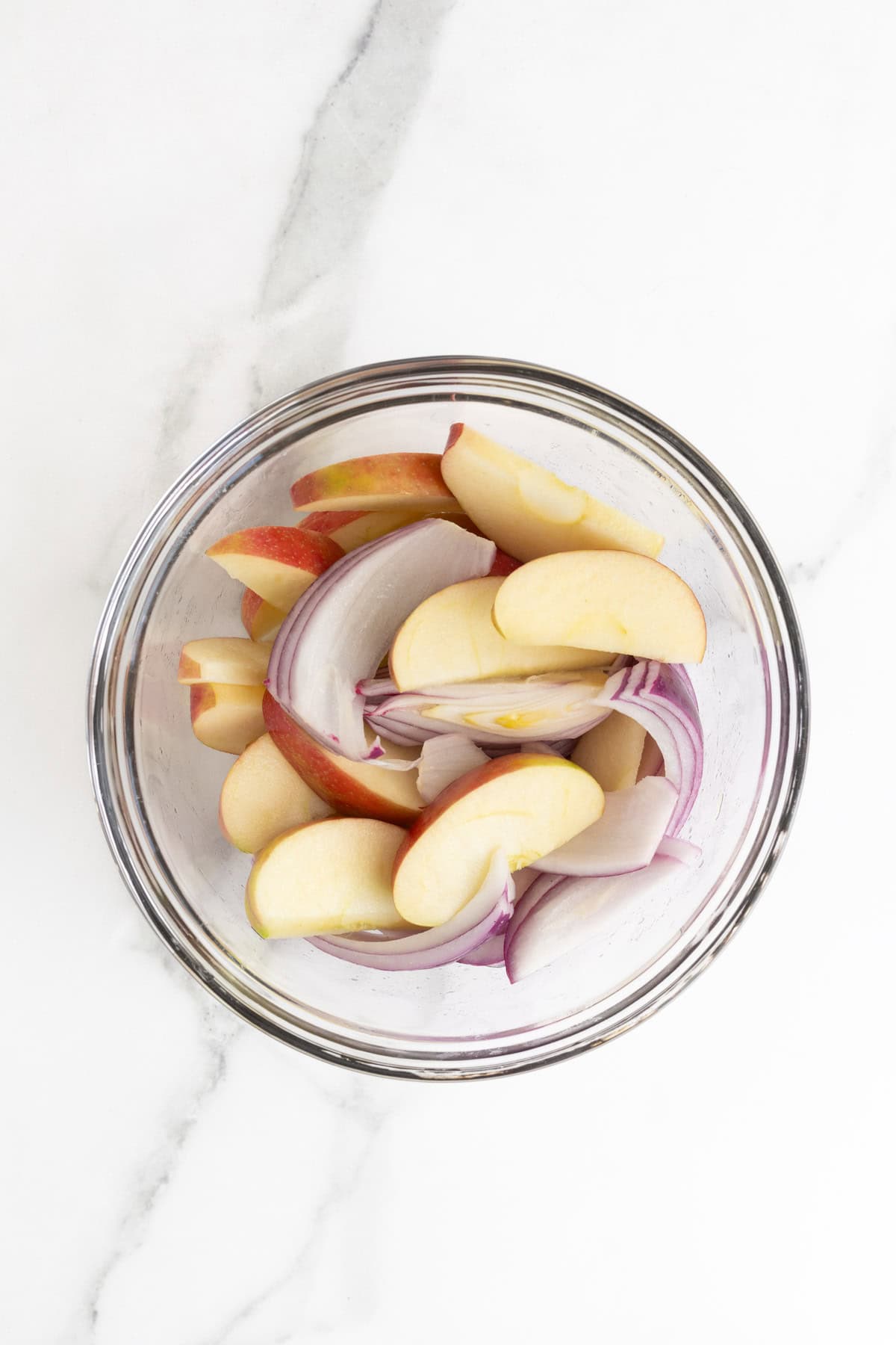Apples and onions tossed in marinade in a glass bowl