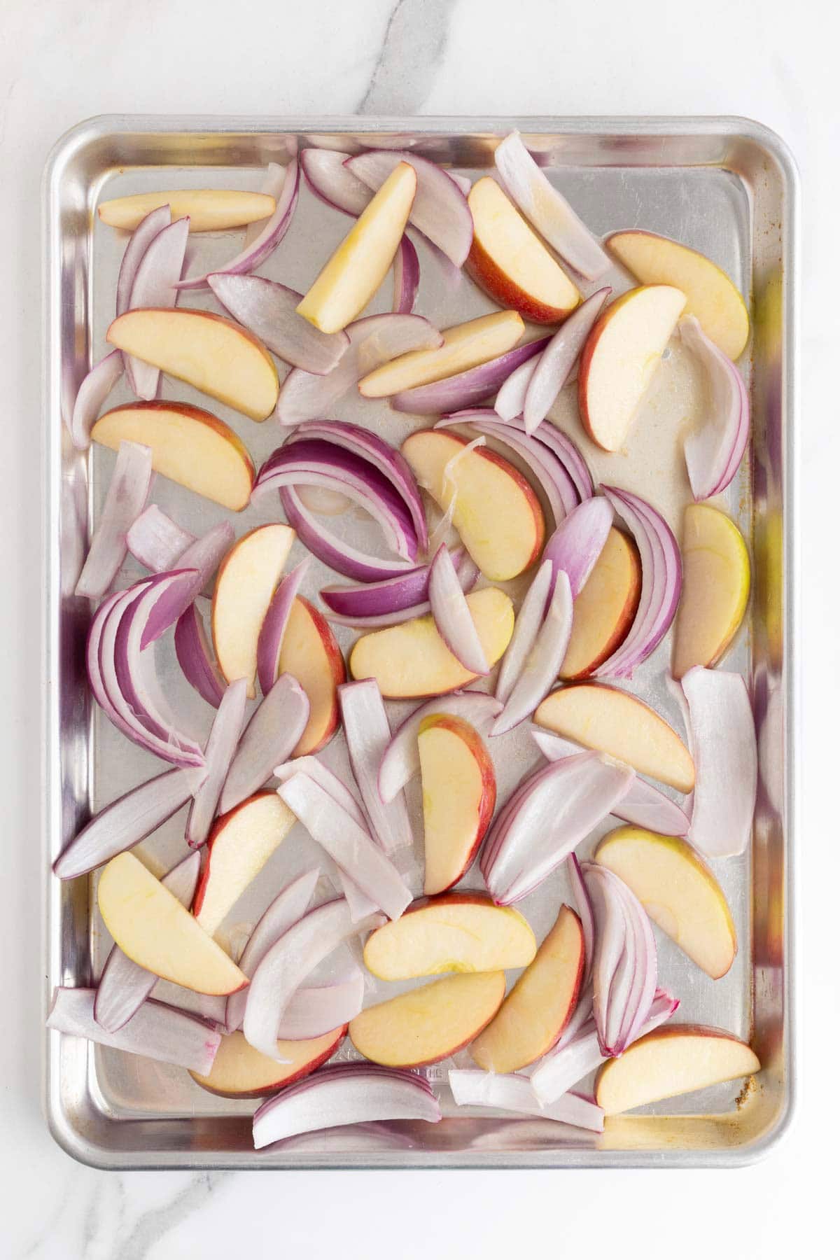 Apples and onions arranged on a sheet pan, ready to roast