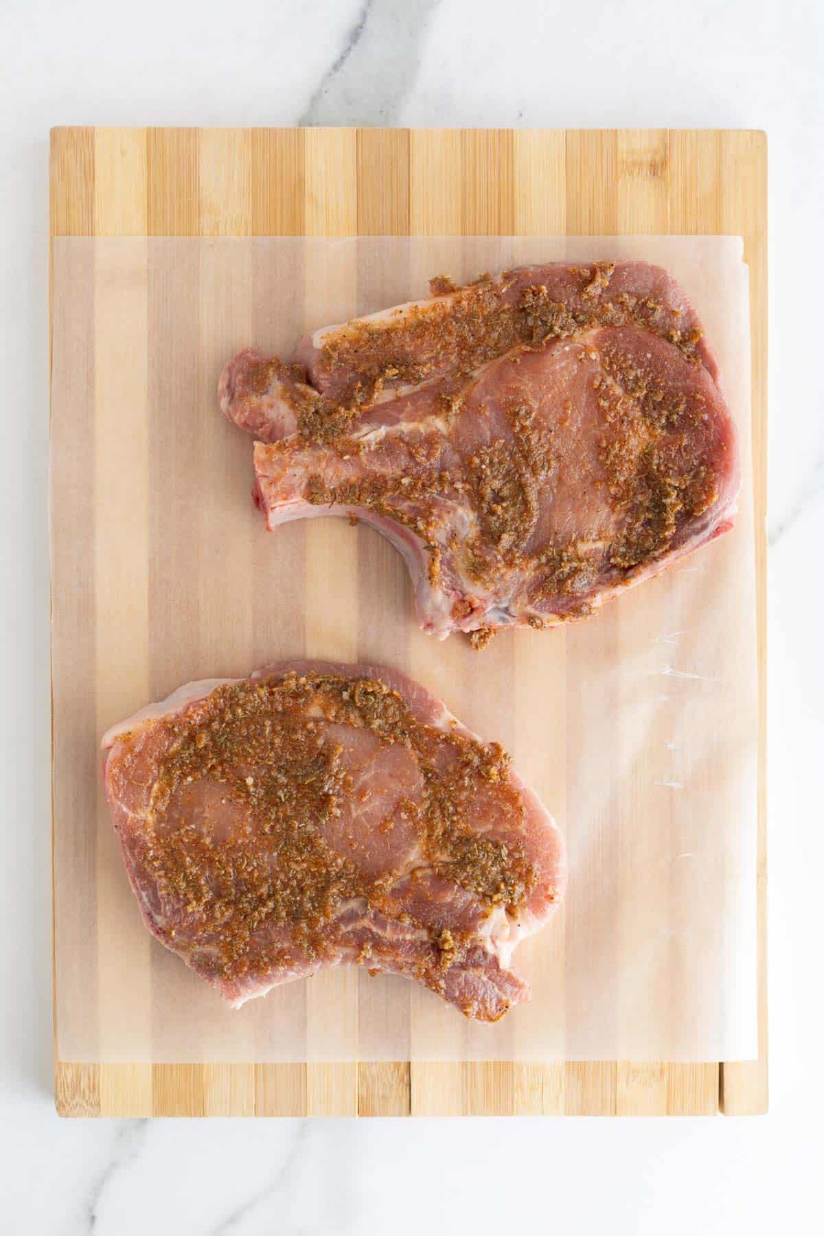 Raw bone-in pork chops coated with spice rub on parchment