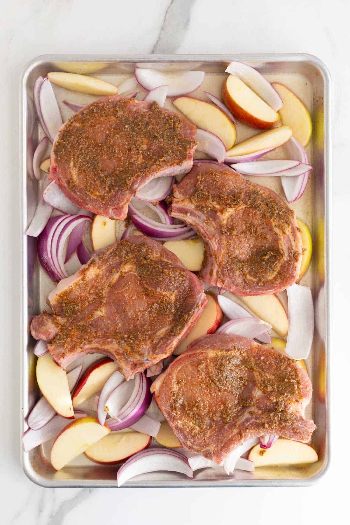 Seasoned pork chops layered over apples and onions on a sheet pan