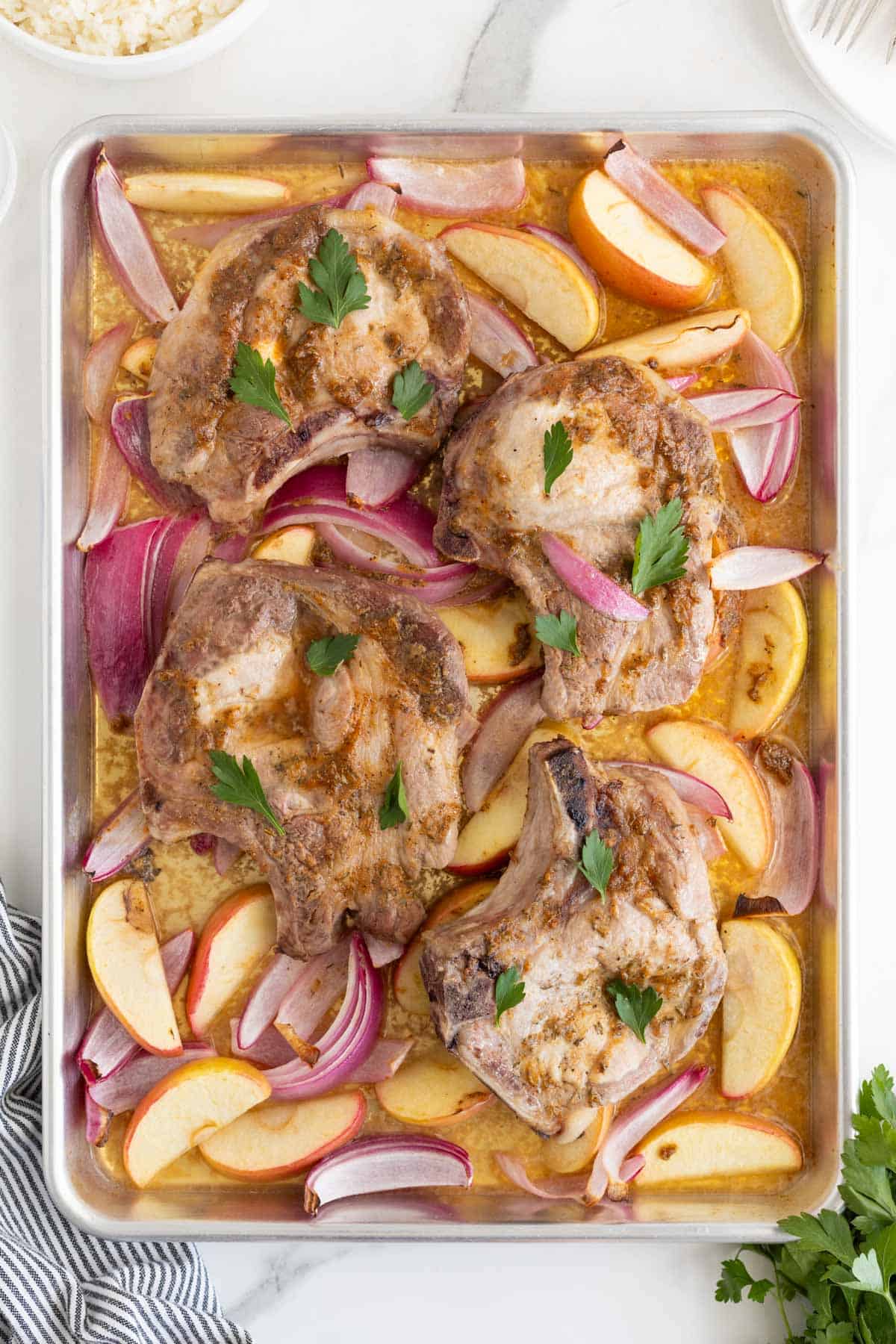 Fully baked sheet pan pork chops with apples and onions, garnished with parsley