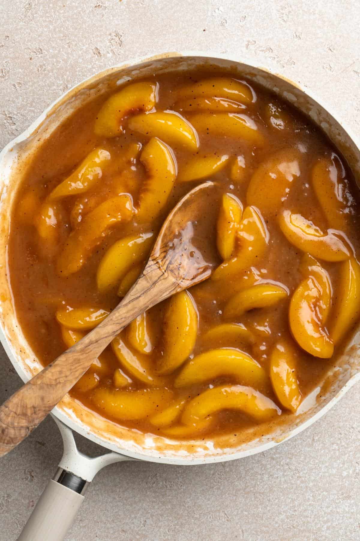 Thickened peach cobbler filling with a wooden spoon resting in the saucepan