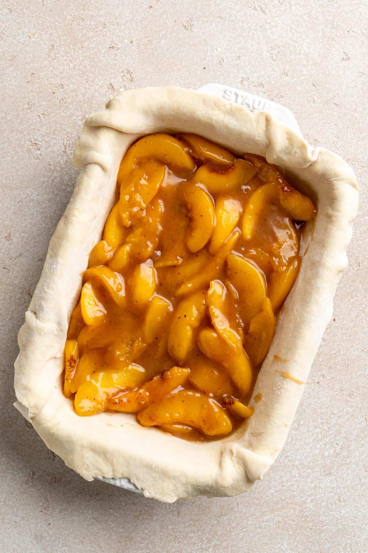 Unbaked Southern peach cobbler with spiced peach filling and folded pie crust in a white baking dish