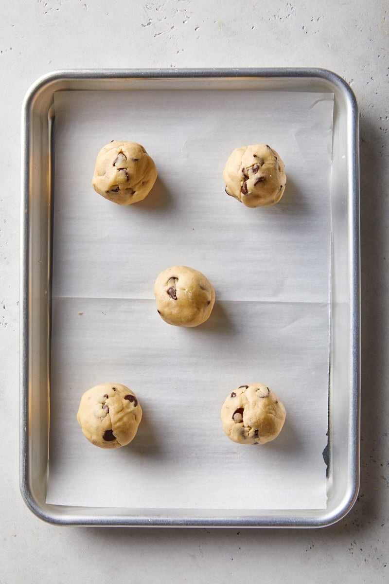 Caramel pieces enclosed inside balls of chocolate chip cookie dough on a lined baking sheet