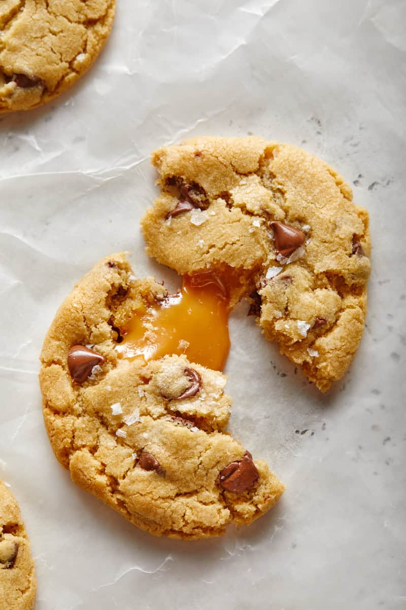 Closeup of a salted caramel chocolate chip cookie broken open with gooey caramel spilling from the center