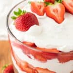 Layered strawberry trifle in a glass bowl with strawberry cake, cream, and strawberries