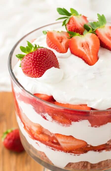 Layered strawberry trifle in a glass bowl with strawberry cake, cream, and strawberries