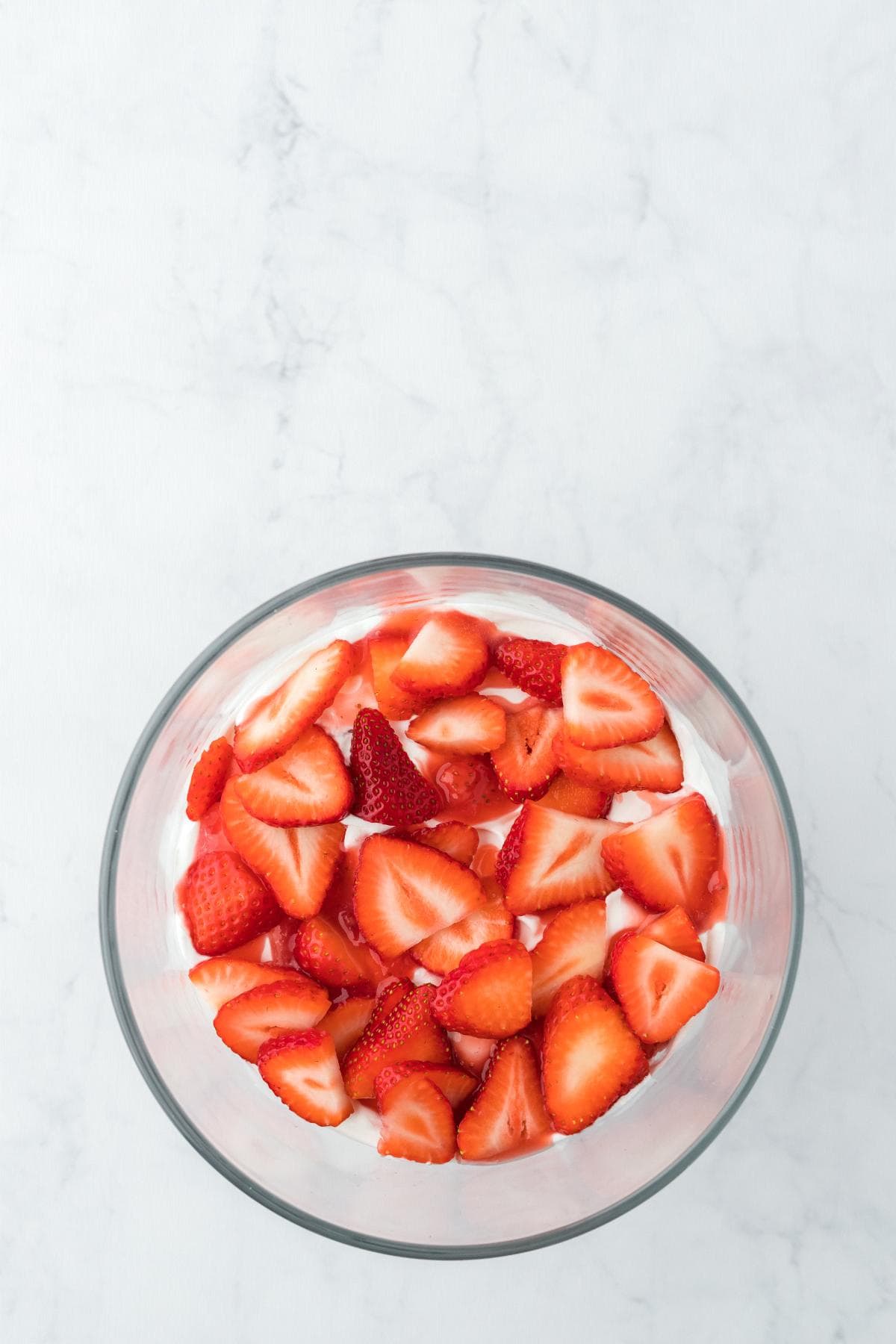 Fresh sliced strawberries layered over whipped cream in a bowl