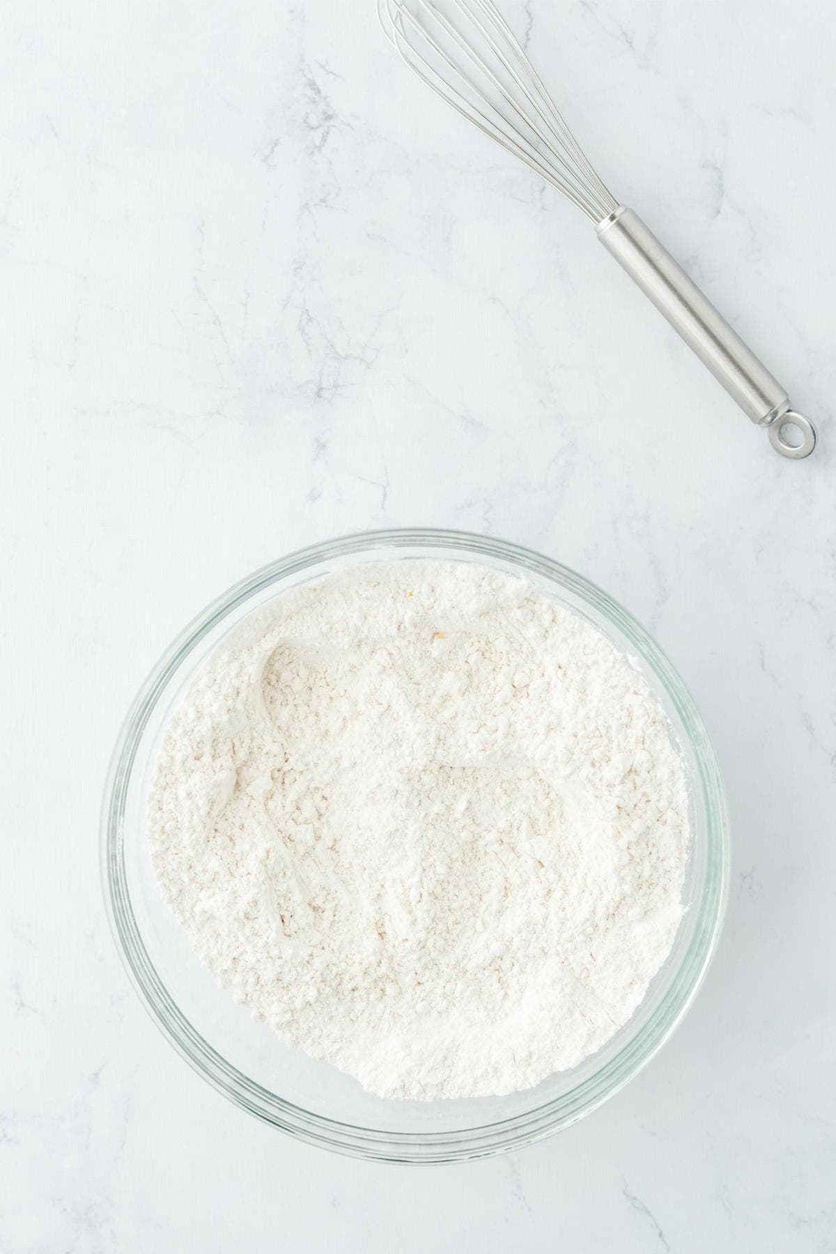 Bowl of dry ingredients with whisk on a white surface