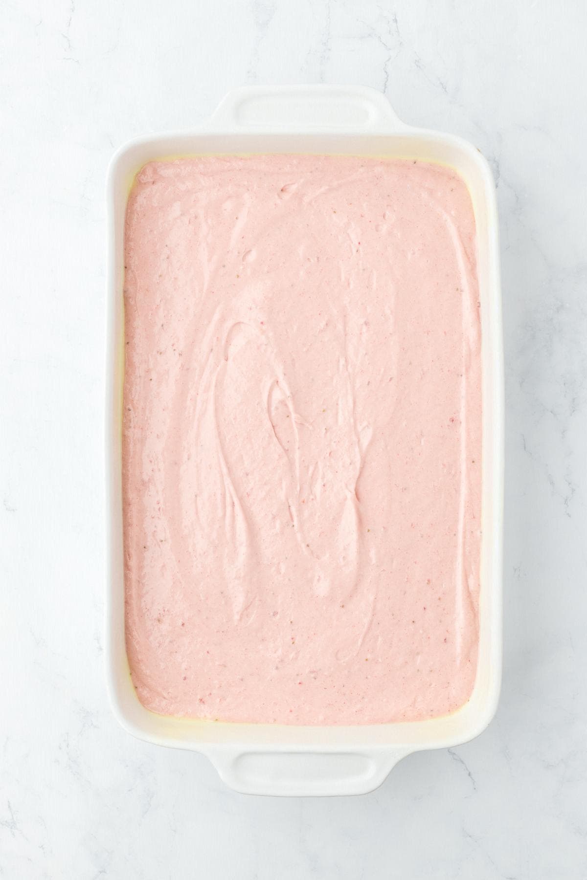 Pink strawberry batter spread evenly in a baking dish