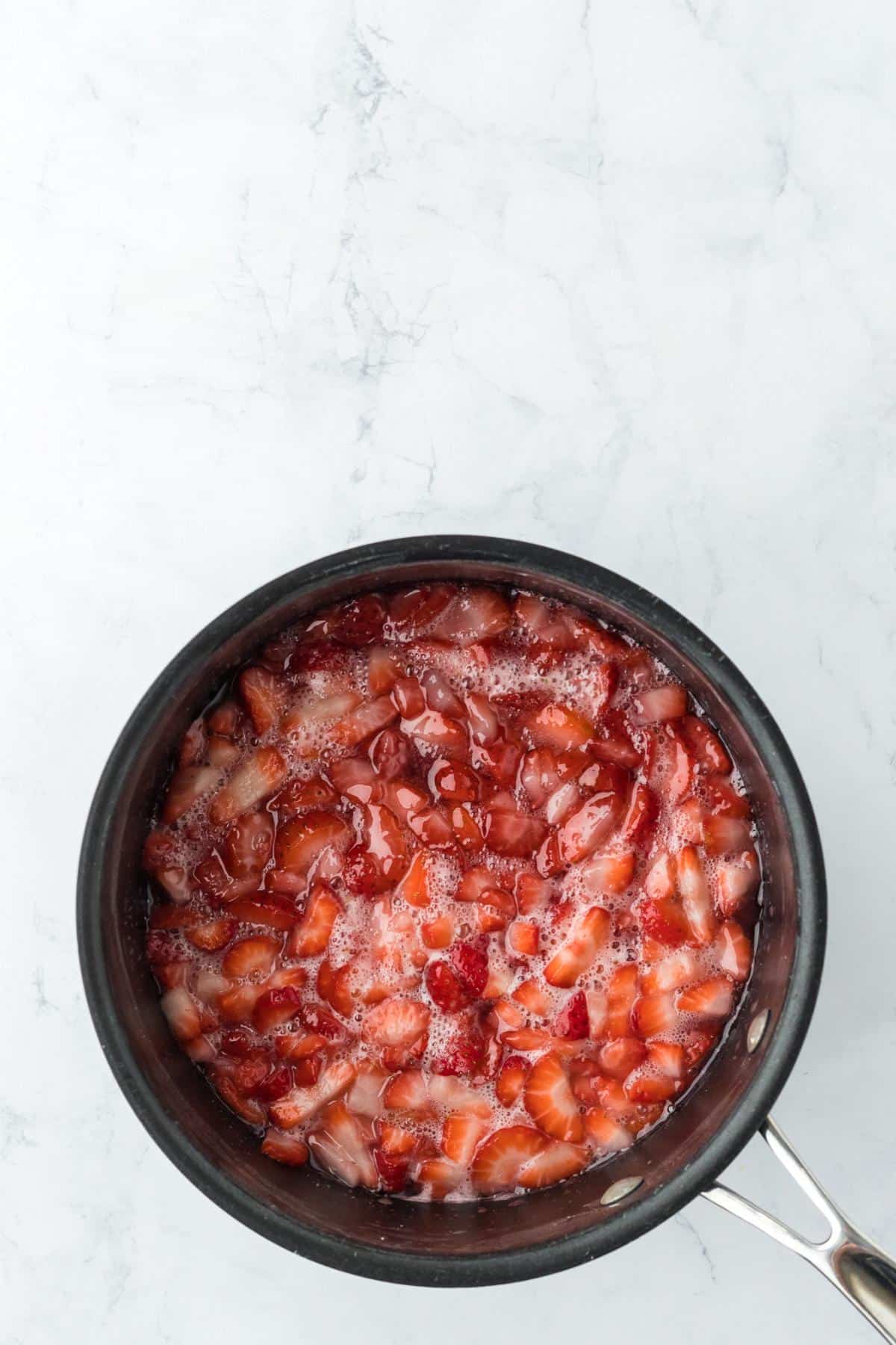 Chopped strawberries simmering in a saucepan with sugar, starting to release juices