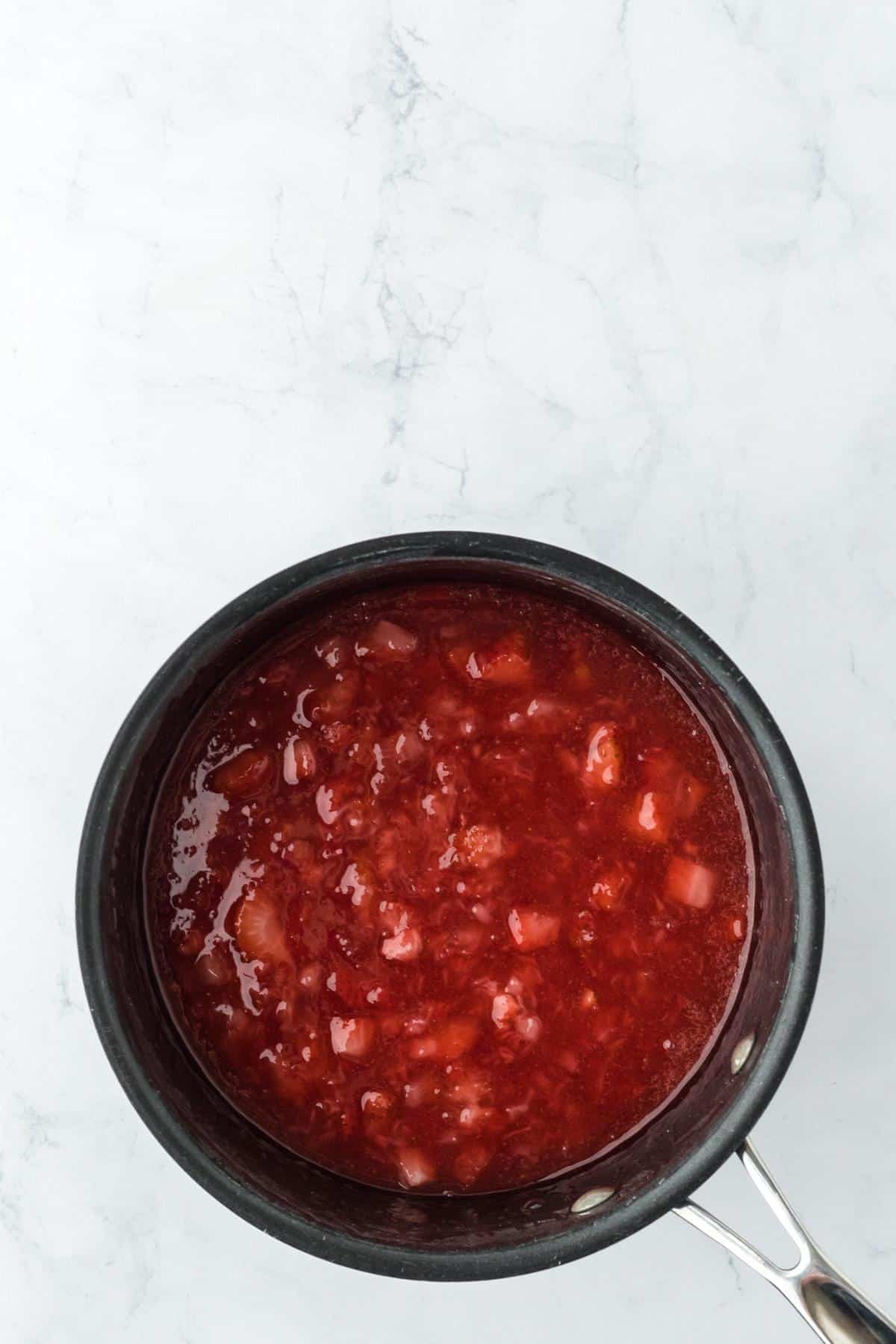 Thickened strawberry sauce cooking in a saucepan until glossy and jammy