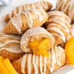 Closeup of a halved peach fried pie with glossy peach filling oozing out, surrounded by more pies and peach slices