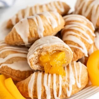 Closeup of a halved peach fried pie with glossy peach filling oozing out, surrounded by more pies and peach slices