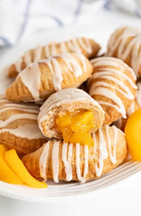 Closeup of a halved peach fried pie with glossy peach filling oozing out, surrounded by more pies and peach slices