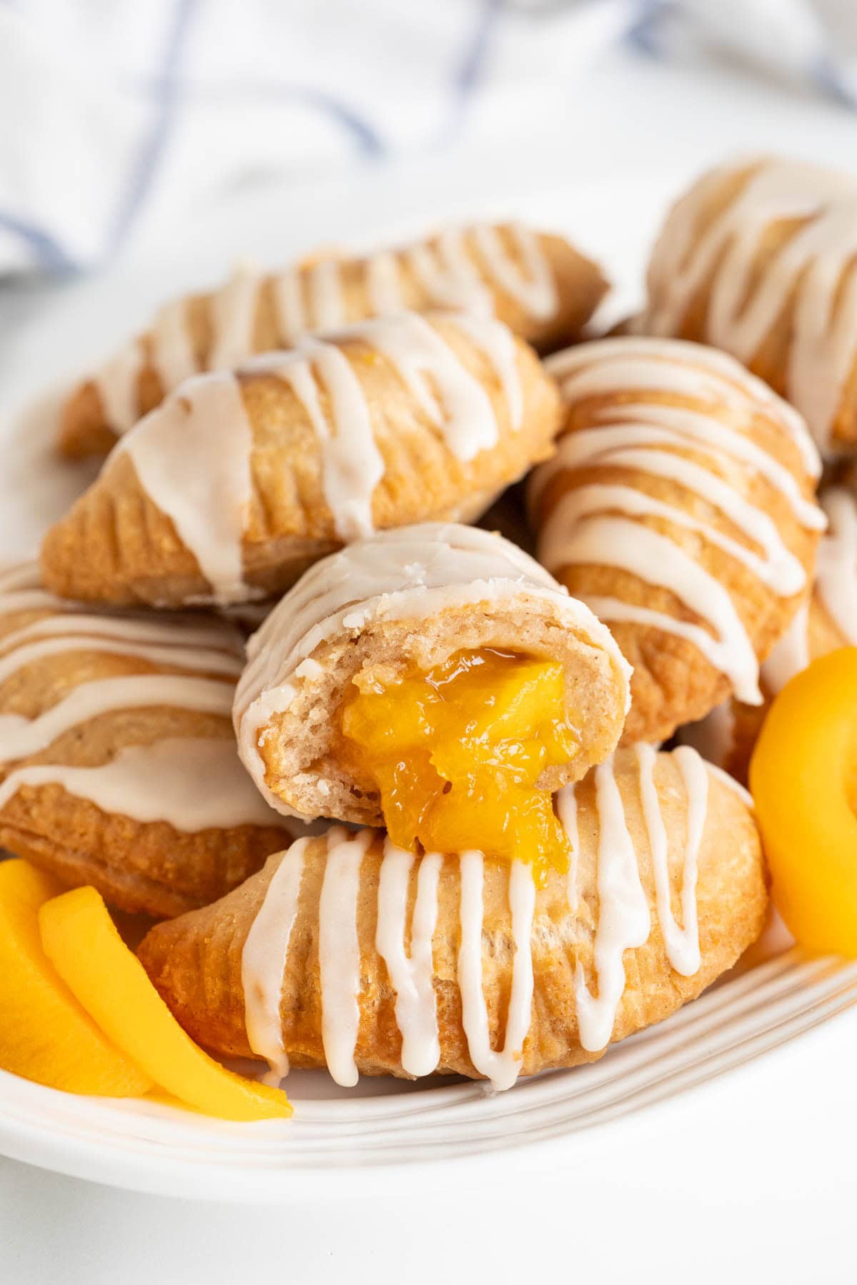 Closeup of a halved peach fried pie with glossy peach filling oozing out, surrounded by more pies and peach slices