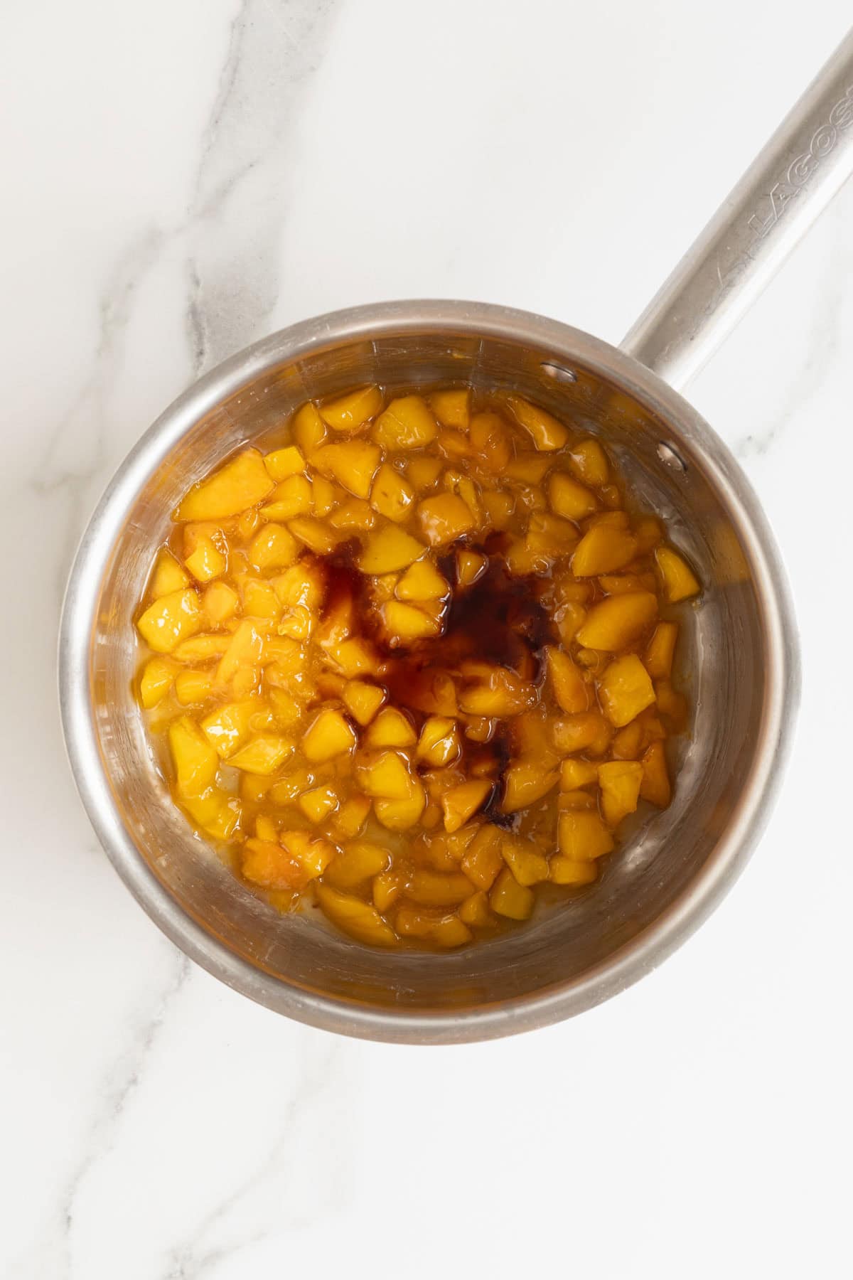 Peach filling simmering in a saucepan with vanilla extract added on top