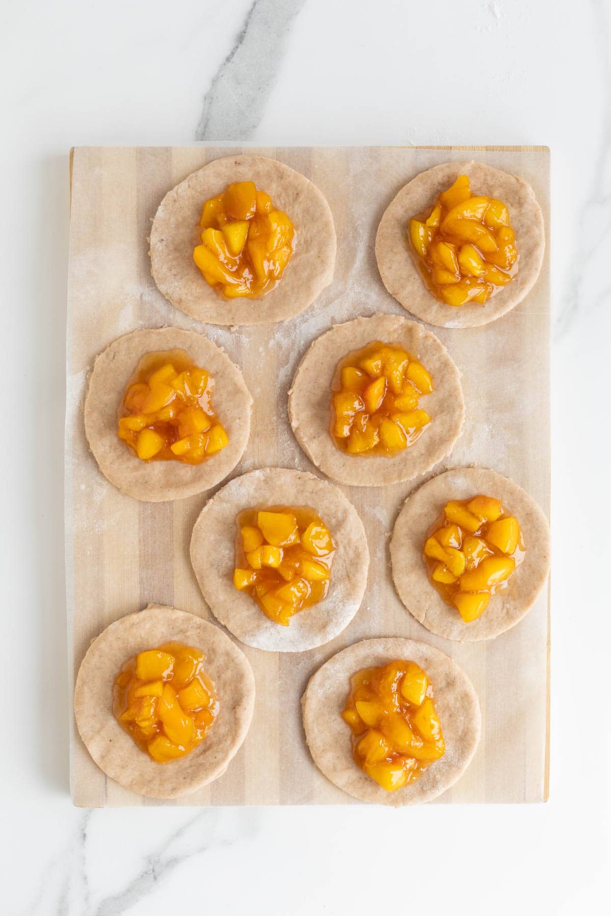 Dough circles topped with peach filling, ready to be folded