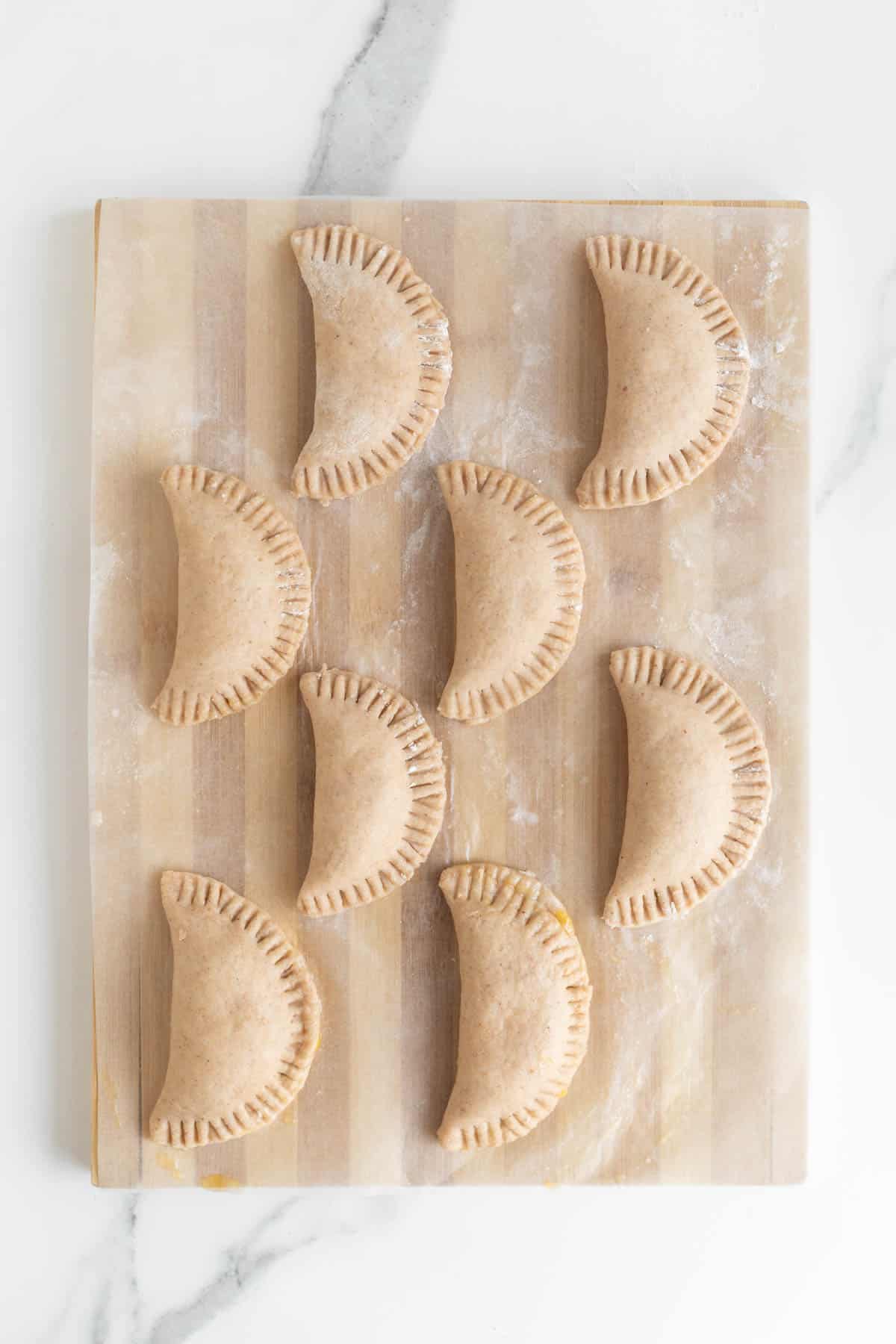 Sealed peach hand pies on a wooden board, crimped edges visible