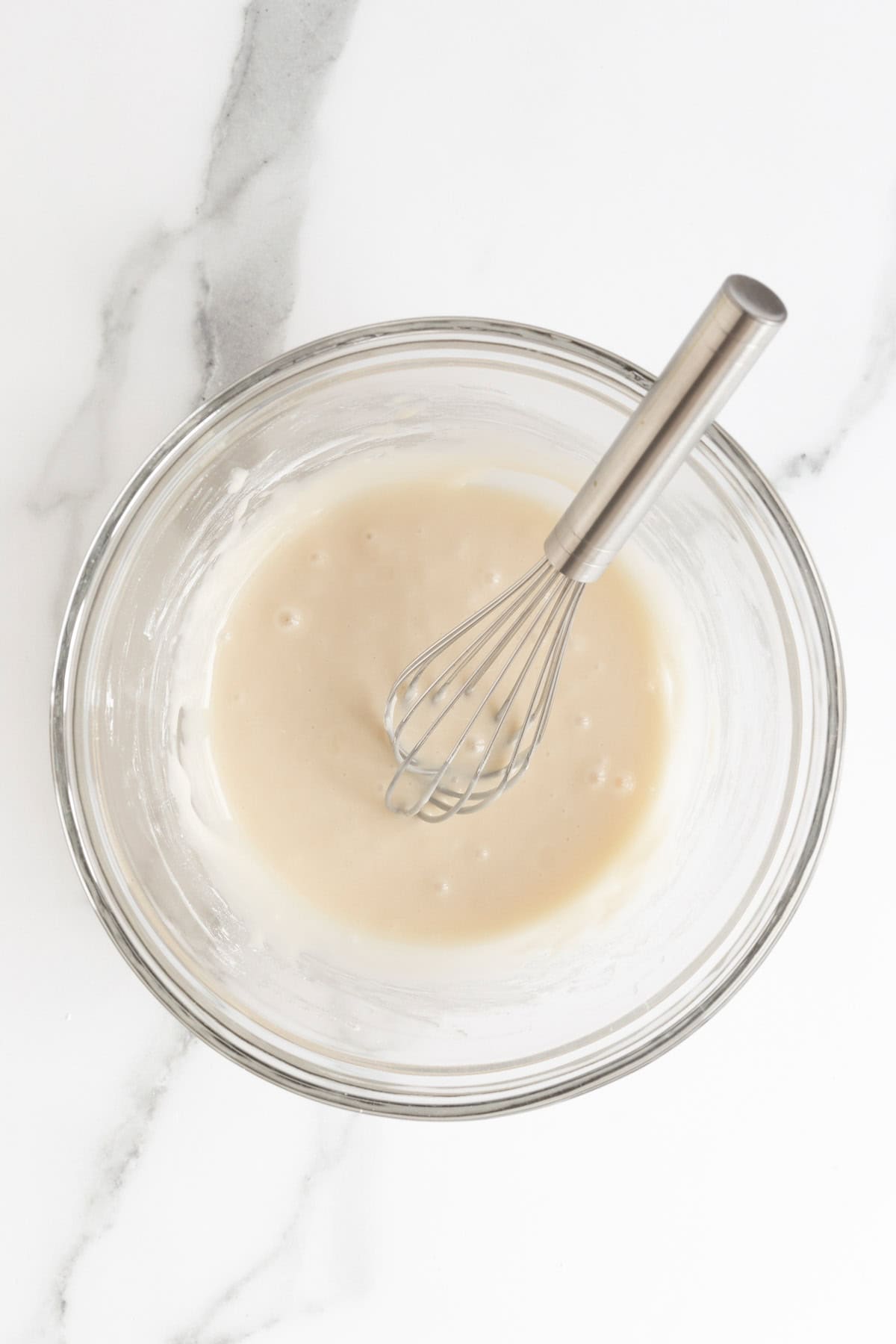 Smooth vanilla glaze whisked together in a clear mixing bowl