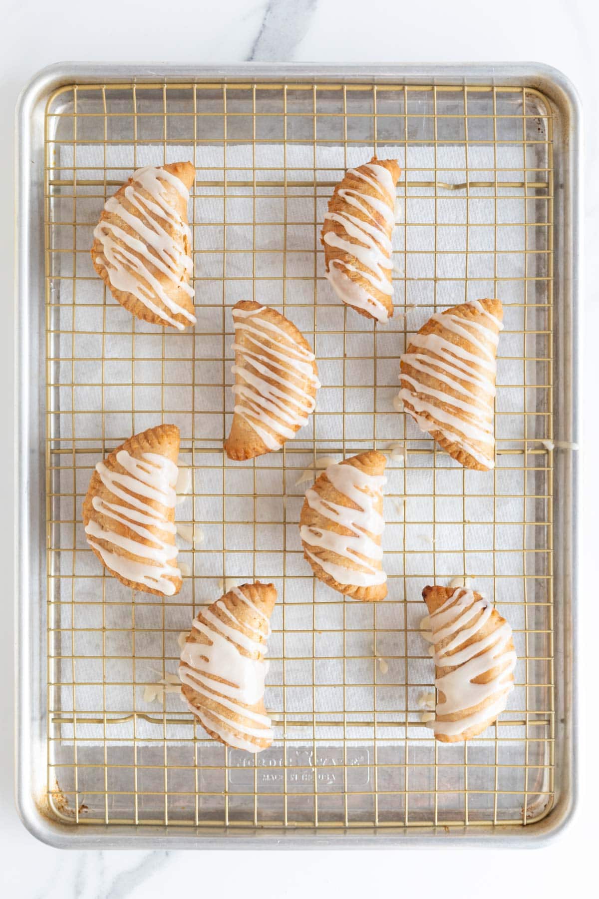 Finished peach fried pies on a wire rack with glaze drizzled on top