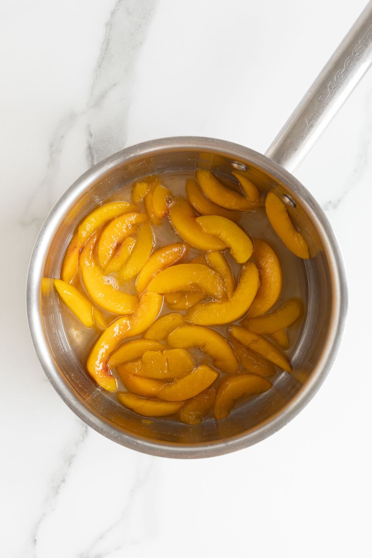 Peaches cooking in their juices with lemon juice, creating a syrupy mixture