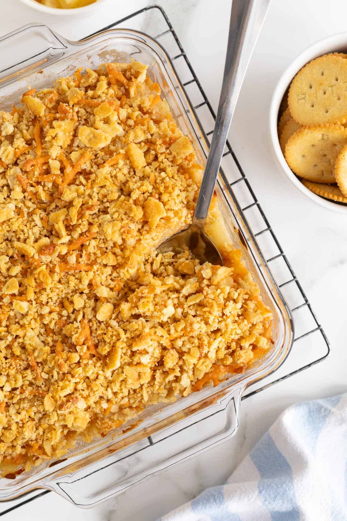 Overhead shot of a pineapple casserole with a spoon in it, sitting on a cooling rack