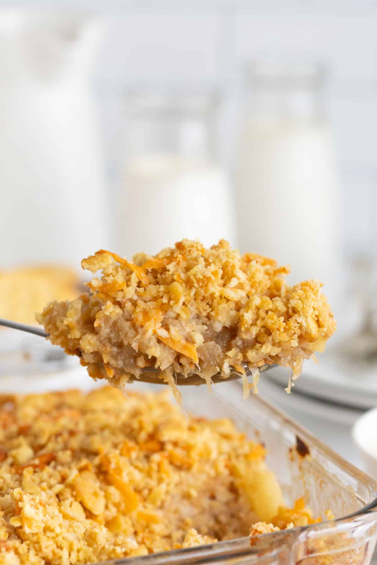 Closeup of a serving spoon scooping out a portion of pineapple casserole, showing the filling and crispy topping