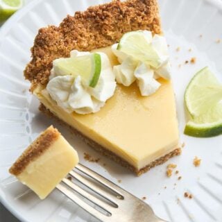 Closeup of a plated slice of key lime pie with whipped cream, lime garnish, and a fork with a bite ready to eat