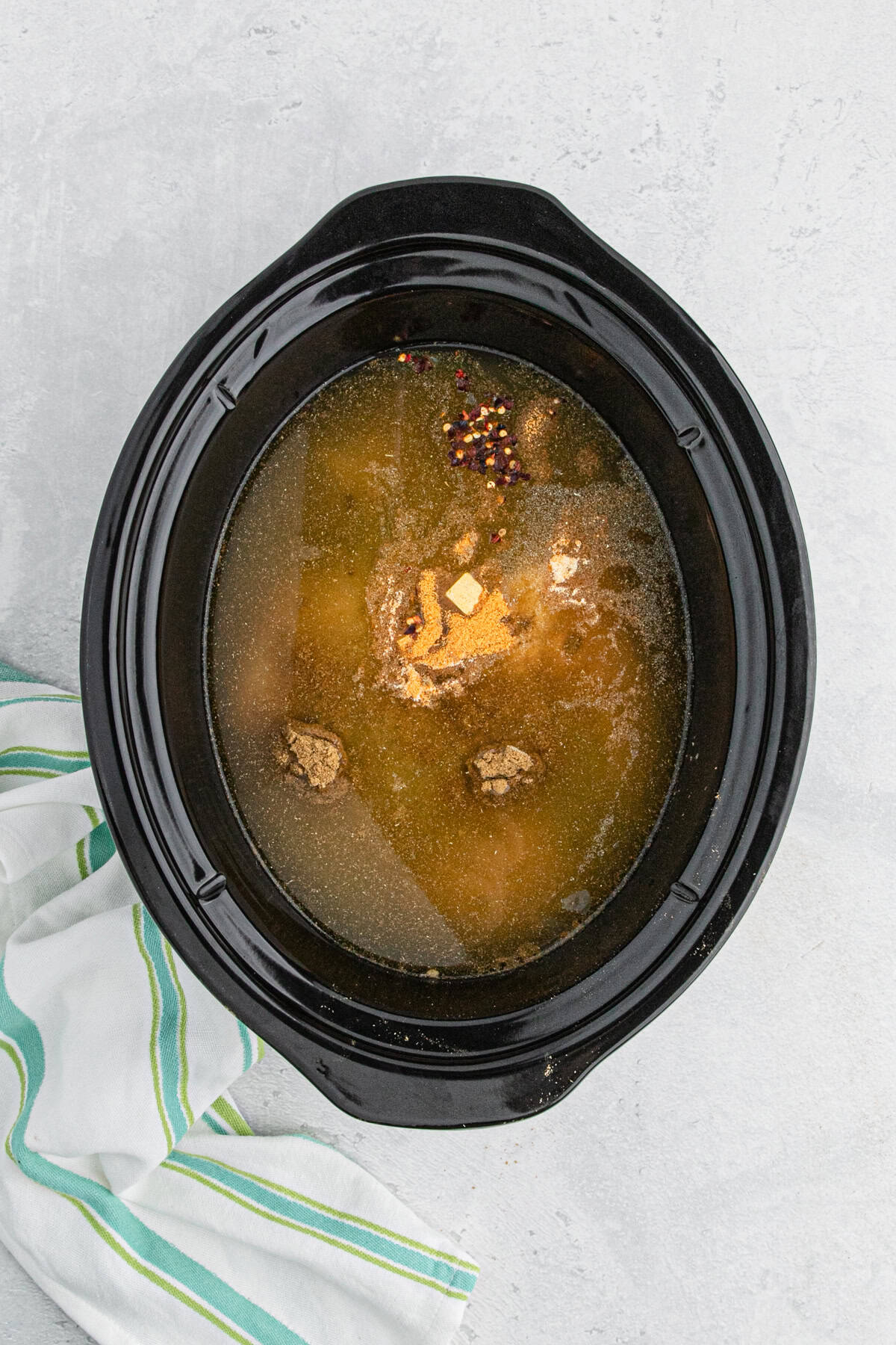 Slow cooker with broth, chicken, and seasonings before cooking