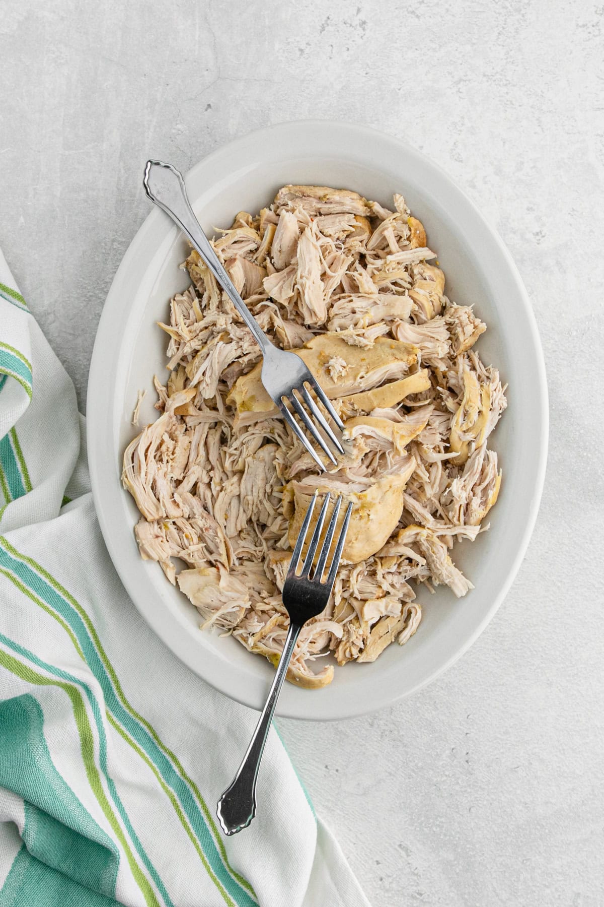 Shredded cooked chicken in a white dish with two forks resting on top